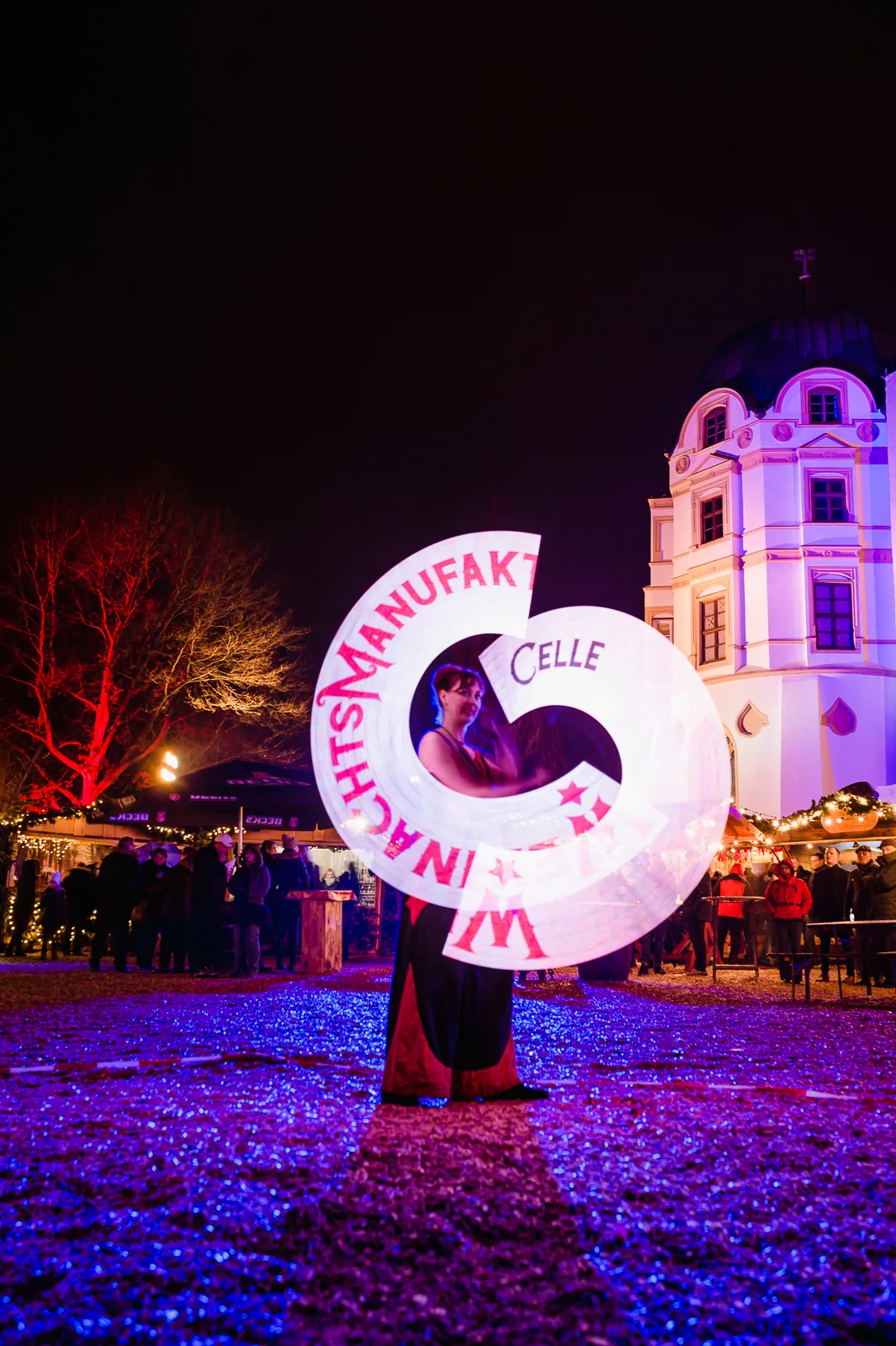 Personalisierte LED-Lichtshow von Elements of Fire mit dem hell leuchtenden Schriftzug Weihnachtsmanufaktur Celle vor dem Celler Schloss bei Nacht.